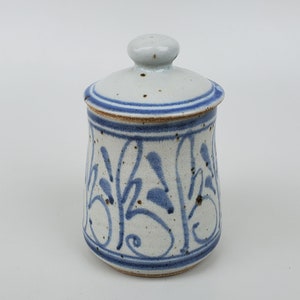 May include: A white ceramic jar with a blue and white floral design. The jar has a lid and is approximately 4 inches tall.