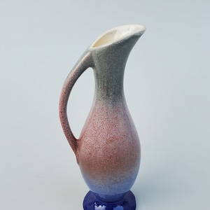 May include: A small ceramic vase with a blue, red, and gray ombre glaze. The vase has a rounded body and a flared lip. The base is a solid blue color.