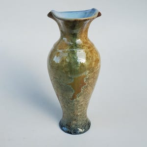 May include: A handcrafted ceramic vase with a unique crystalline glaze. The vase features a flared rim with a light blue interior, transitioning to a warm brown and green exterior. The base is a darker, mottled blue-grey. A decorative piece for the home.