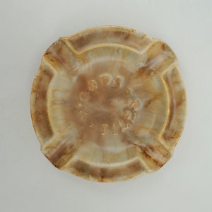 May include: A round, ceramic ashtray with a light brown glaze and a darker brown rim. The ashtray has three indentations for cigarettes and the words "Corps of Engineers" are embossed in the center.