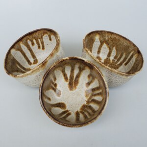 May include: Three white ceramic bowls with brown abstract designs. The bowls are slightly rounded and have a speckled glaze.