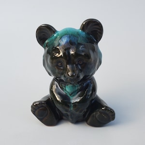 May include: A small ceramic bear figurine with a black and green glaze. The bear is sitting with its paws in front of it.