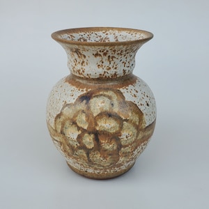 May include: A white ceramic vase with a brown and white speckled glaze. The vase has a wide mouth and a rounded body.