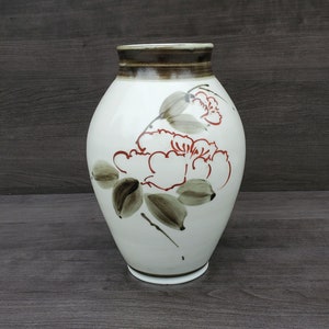 May include: White ceramic vase with a brown rim and floral design. The vase features red and brown flowers with green leaves.