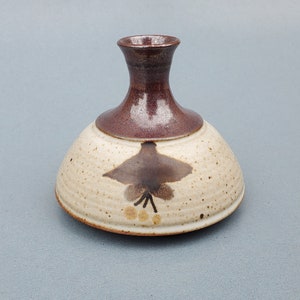 May include: A small, brown and white ceramic vase with a wide base and a narrow neck. The vase has a brown glaze with a floral design.