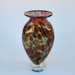 May include: A brown and green glass vase with a swirling pattern. The vase has a wide mouth and a narrow base.