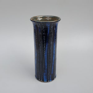 May include: A tall, cylindrical ceramic vase with a blue and black glaze. The vase has a textured surface with vertical lines.