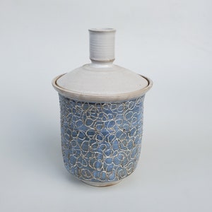 May include: A white ceramic jar with a lid, featuring a blue and white floral pattern. The jar has a simple, elegant design.