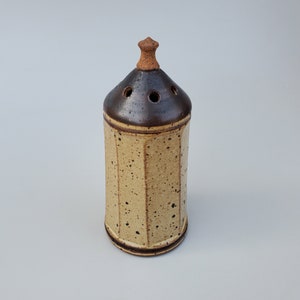 May include: A ceramic salt cellar with a brown lid and a speckled beige body. The lid has a small knob on top.