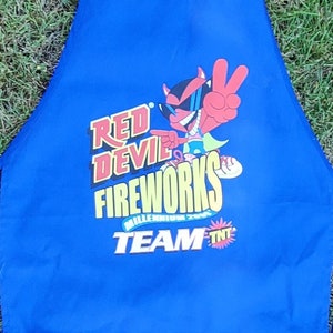 May include: Blue apron with a red devil character and the text "Red Devil Fireworks Team TNT".
