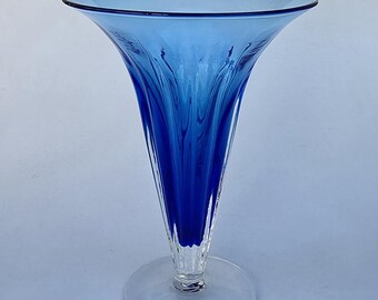 May include: A tall, elegant blue glass vase with a flared top and a clear, circular base. The vase has a slender, conical shape with vertical, textured lines. The blue color is a deep, rich shade.