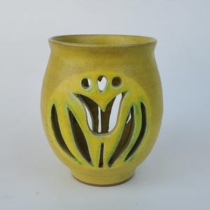 May include: A yellow ceramic vase with a tulip-shaped cutout design. The vase has a rounded body and a slightly flared rim. The cutout reveals a green interior, adding a pop of color. The vase is approximately 7 inches tall.