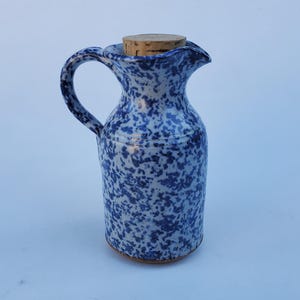 May include: A blue and white ceramic pitcher with a cork stopper. The pitcher has a speckled blue and white glaze.