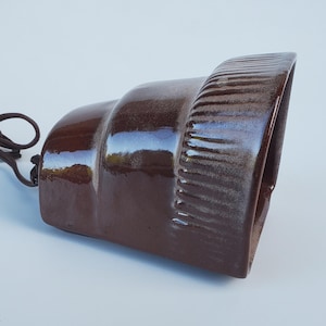 May include: A brown ceramic lampshade with a textured, ribbed design. The lampshade has a cord attached to it.