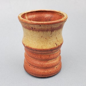 May include: A ceramic vase with a textured, ribbed design. The vase is glazed in shades of brown and yellow.