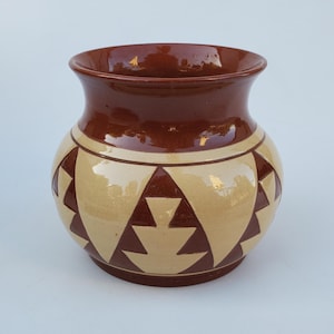 May include: A brown ceramic vase with a geometric pattern of triangles in cream and brown. The vase has a rounded body and a wide opening.