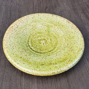 May include: A green ceramic plate with a speckled glaze and a raised centre. The plate is ideal for serving snacks or appetisers.