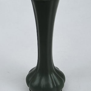 May include: Dark green ceramic vase with a fluted body and a bulbous base. The vase has a narrow neck and a round opening. The base has a scalloped design. The vase is a solid color and has a matte finish.
