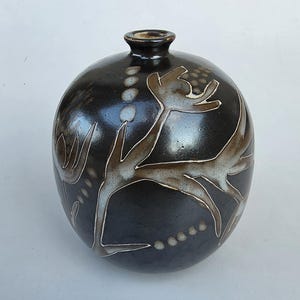 May include: A round ceramic vase with a glossy dark brown glaze. The surface features etched floral patterns and dotted lines in a lighter tan and cream color, revealing the clay body beneath. The vase has a narrow neck and a small circular opening.