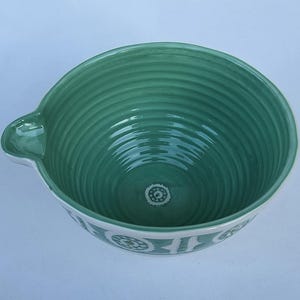 Peut inclure: Un saladier en c&eacute;ramique turquoise avec un bord blanc et un bec verseur. L'int&eacute;rieur pr&eacute;sente des rainures concentriques et un motif floral d&eacute;coratif au fond. L'ext&eacute;rieur a une bande blanche avec un motif floral r&eacute;p&eacute;t&eacute;.