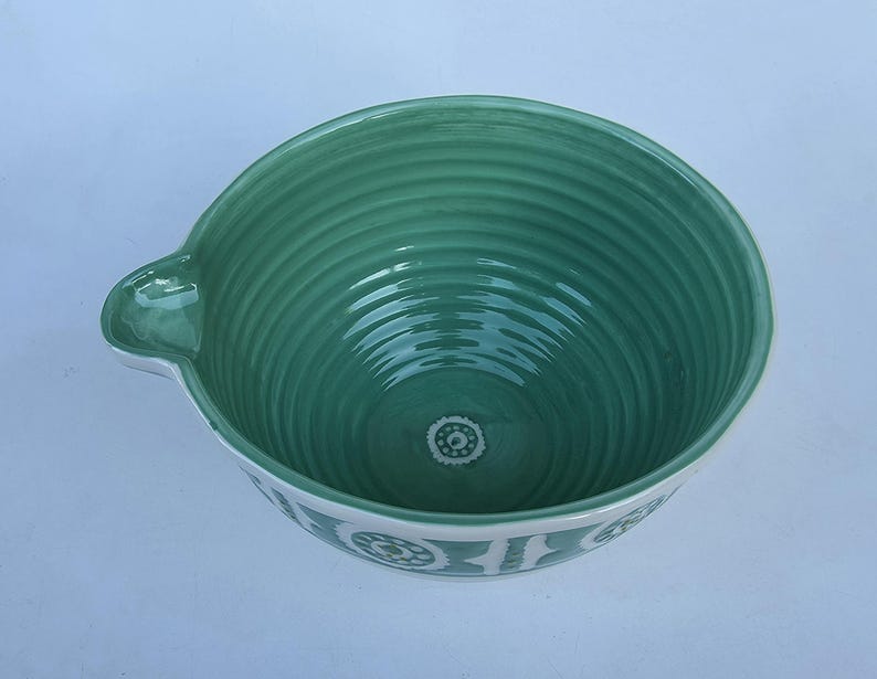 Peut inclure: Un saladier en c&eacute;ramique turquoise avec un bord blanc et un bec verseur. L'int&eacute;rieur pr&eacute;sente des rainures concentriques et un motif floral d&eacute;coratif au fond. L'ext&eacute;rieur a une bande blanche avec un motif floral r&eacute;p&eacute;t&eacute;.