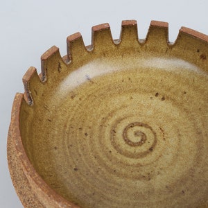 May include: A brown ceramic ashtray with a scalloped edge and a spiral design in the center.