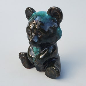 May include: A black ceramic bear figurine with a teal glaze. The bear is sitting with its paws tucked in front of it.