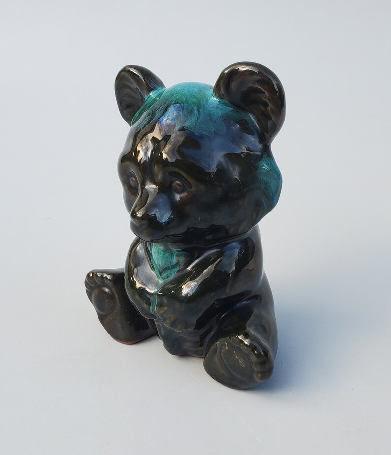 May include: A black ceramic bear figurine with a teal glaze. The bear is sitting with its paws tucked in front of it.