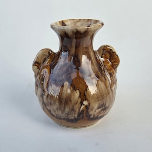 May include: A ceramic vase with a glossy finish featuring a marbled pattern of dark brown, tan, and cream colors. The vase has a rounded body, a flared rim, and two small, curved handles attached to the sides of the neck area.