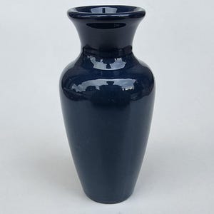 May include: A navy blue ceramic vase with a glossy finish. The vase has a flared rim and a rounded body that tapers towards the base. The vase is approximately 10 inches tall.