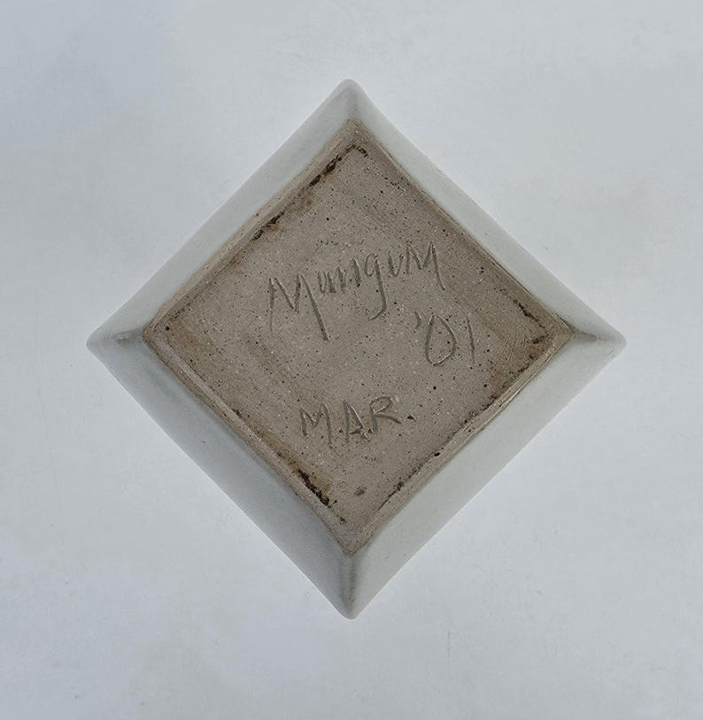 May include: A white ceramic dish with a diamond shape. The bottom of the dish has the handwritten text "Mungum '01 MAR."