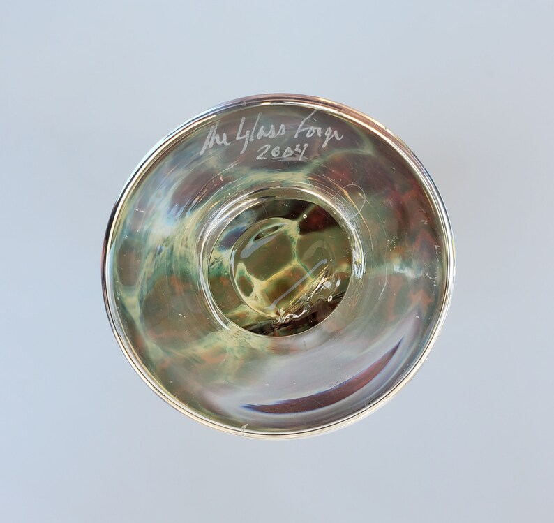 May include: The underside of a clear glass bowl with a swirling pattern. The bowl is signed "The Glass Forge 2003".