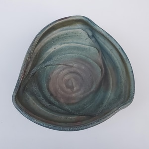 May include: A green and brown ceramic bowl with a swirling pattern. The bowl is handmade and has a unique, organic shape.