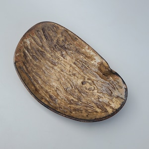 May include: A rustic, oval-shaped ceramic dish with a brown and white glaze. The dish has a textured surface that resembles wood grain.
