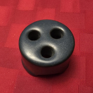 May include: A dark blue, cylindrical object with three circular holes on top. The object is sitting on a red checkered surface. The object appears to be made of a solid material.