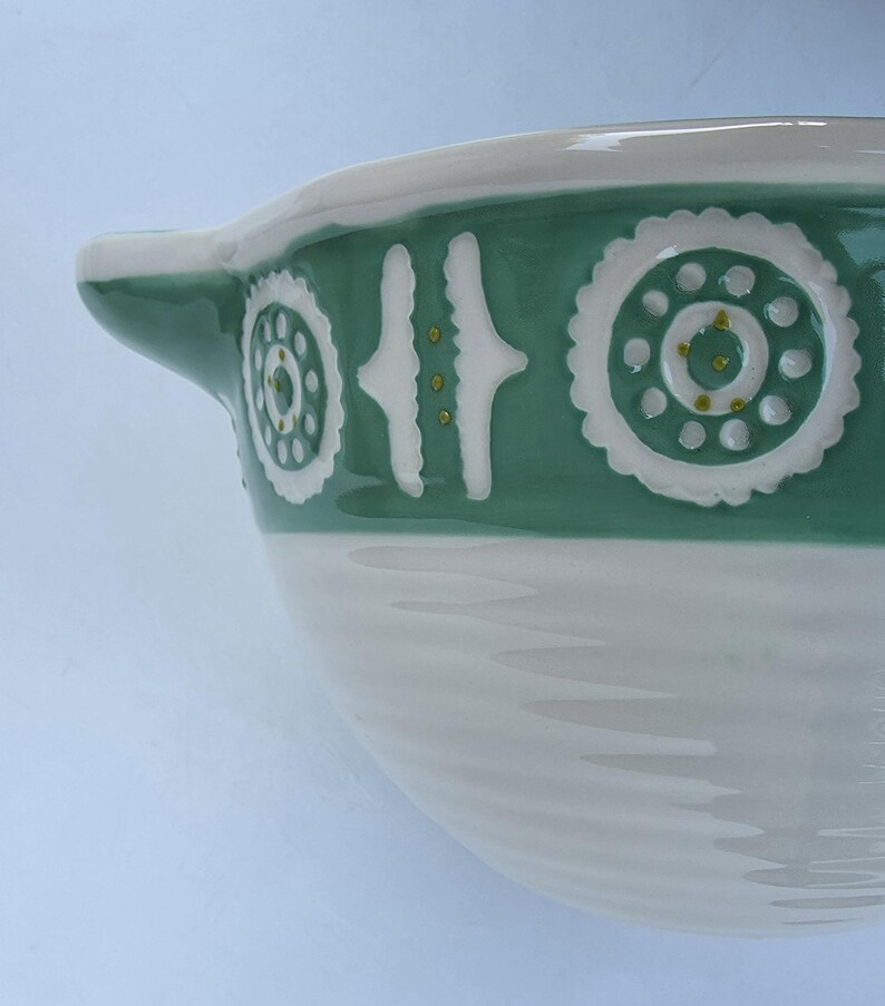 Peut inclure: Un bol en c&eacute;ramique blanc et vert avec une anse. Le bol pr&eacute;sente une bande d&eacute;corative verte avec des accents blancs et dor&eacute;s. La partie inf&eacute;rieure du bol est blanche avec un motif textur&eacute; et nervur&eacute;.