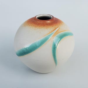 May include: A white ceramic vase with a rounded shape and a brown rim. The vase has a teal glaze design with a wavy pattern.