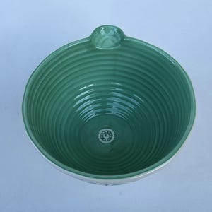 Peut inclure: Un bol en c&eacute;ramique turquoise avec un int&eacute;rieur textur&eacute; et stri&eacute;. Le bol a une petite poign&eacute;e et un bord blanc. Un petit motif floral d&eacute;coratif est visible au centre du fond du bol.
