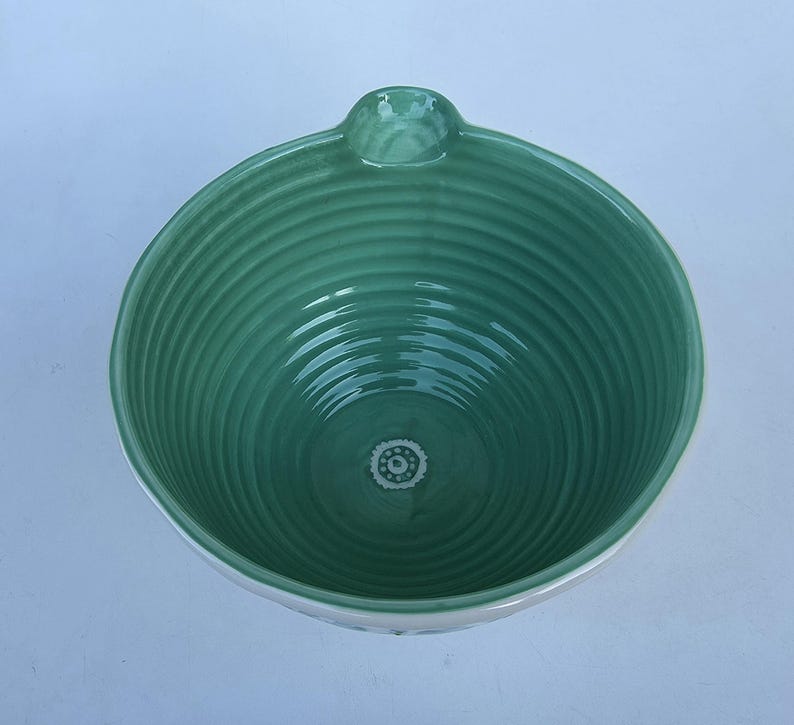 Peut inclure: Un bol en c&eacute;ramique turquoise avec un int&eacute;rieur textur&eacute; et stri&eacute;. Le bol a une petite poign&eacute;e et un bord blanc. Un petit motif floral d&eacute;coratif est visible au centre du fond du bol.