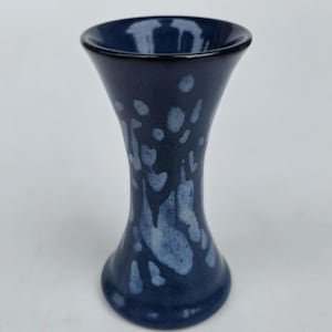 May include: A flared ceramic vase with a deep navy blue glaze featuring a mottled, lighter blue speckled pattern across the body. The vase has a wide, circular opening at the top that tapers inward toward the center before widening at the base.