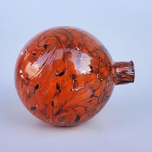 May include: A round, orange glass ornament with a swirling, marbled pattern. The ornament has a small, clear glass opening at the top.