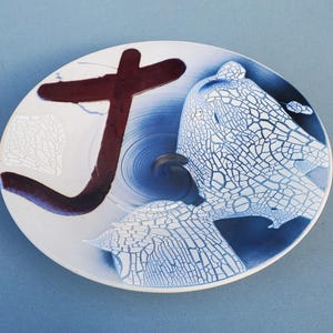May include: White ceramic plate with blue and brown glaze. The plate has a crackled glaze effect and a large brown brushstroke design.