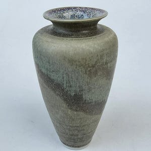 May include: A ceramic vase with a wide base and a narrow neck. The vase has a muted colour palette of grey, green, and brown, with a textured surface. The rim of the vase has a speckled, dark blue and purple glaze.