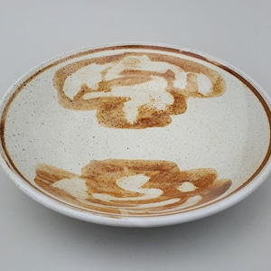 May include: A white ceramic bowl with a brown glaze design. The bowl has a speckled white surface and a brown rim.