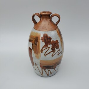 May include: A brown and white ceramic vase with two handles and a geometric design. The vase is decorated with brown and white abstract shapes and a brown leaf pattern.