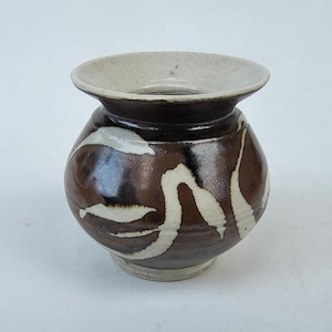 May include: A handcrafted ceramic vase with a bulbous body and a wide, flared rim. The vase features a dark brown glaze with white, abstract, flowing patterns. The rim is a lighter, off-white color. This decorative vase is suitable for home decor.
