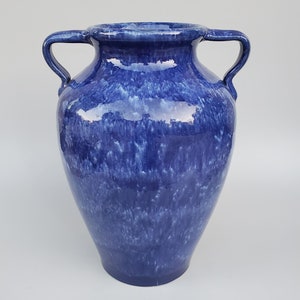 Op de afbeelding: Een blauwe keramische vaas met twee handvatten. De vaas heeft een gevlekt blauwe glazuur met witte strepen.