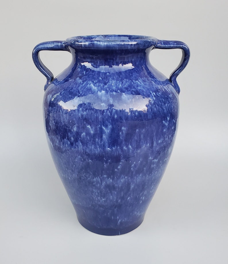 Op de afbeelding: Een blauwe keramische vaas met twee handvatten. De vaas heeft een gevlekt blauwe glazuur met witte strepen.