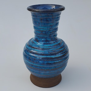 May include: A blue and brown ceramic vase with a wide base and a narrow neck. The vase has a textured, striped design.