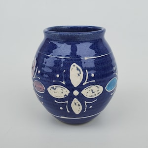 May include: A small, round, blue ceramic vase with white and blue floral designs. The vase has a glossy finish.